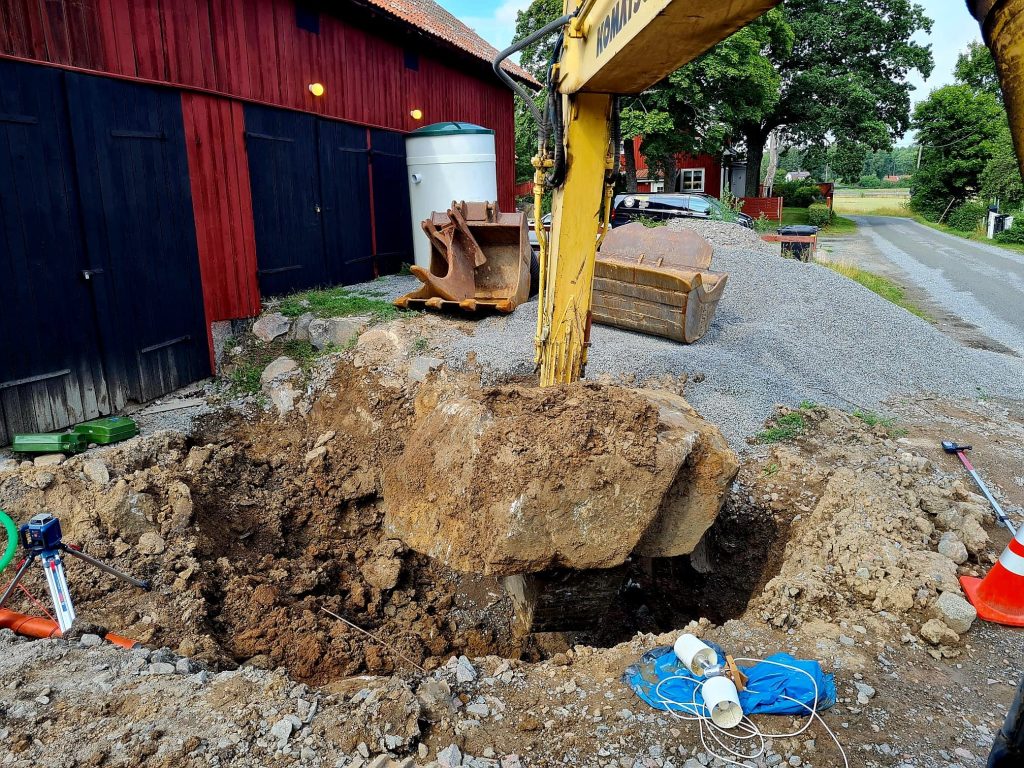 Grävmaskin som lyfter jordmassor vid röd byggnad