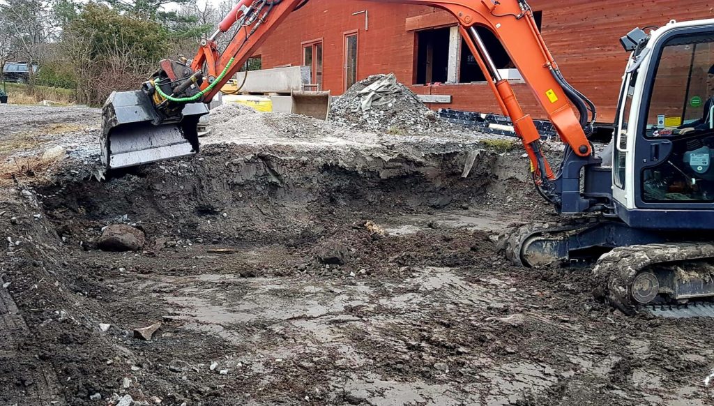 Schaktarbete vid byggnad med orange grävmaskin