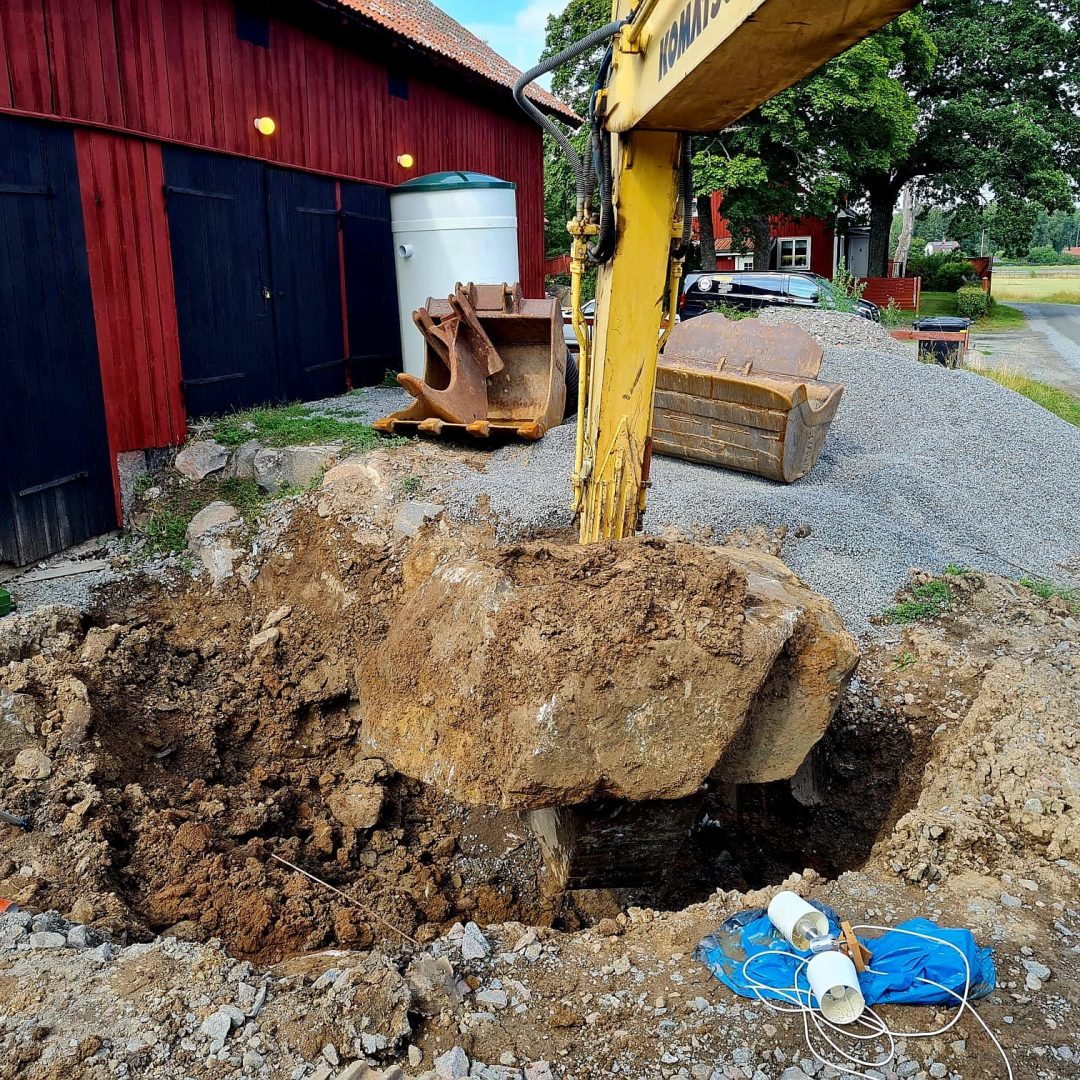 Grävmaskin som lyfter jordmassor vid röd byggnad