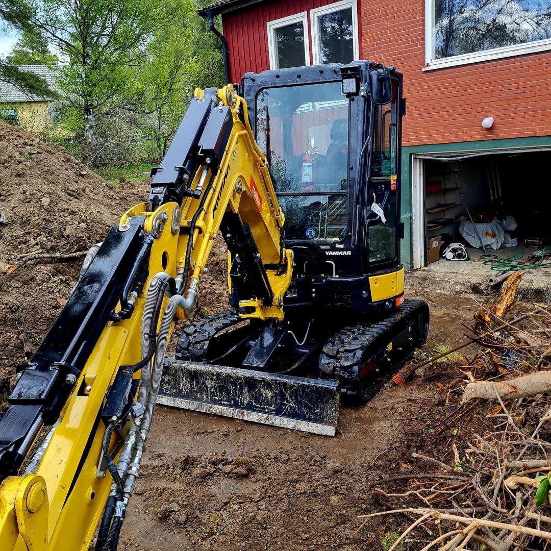 Grävmaskin som gräver vid husgrund och garage.
